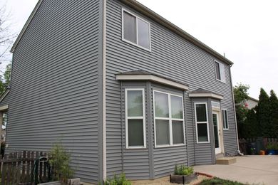 Gray two-story house with bay windows and siding, sitting on a concrete patio.