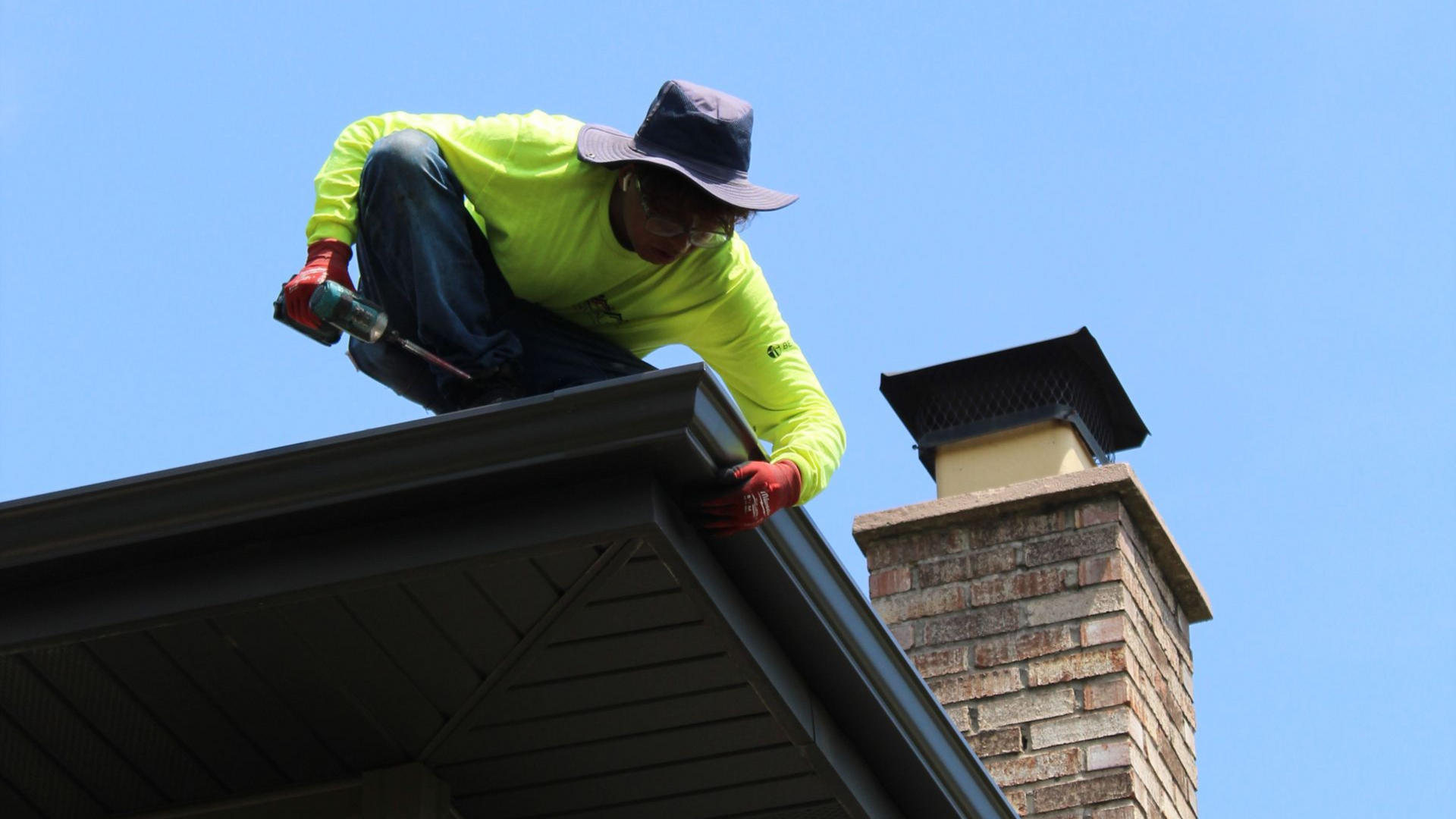 A+ Quality Home Improvement worker installs gutters on a roof near a chimney.