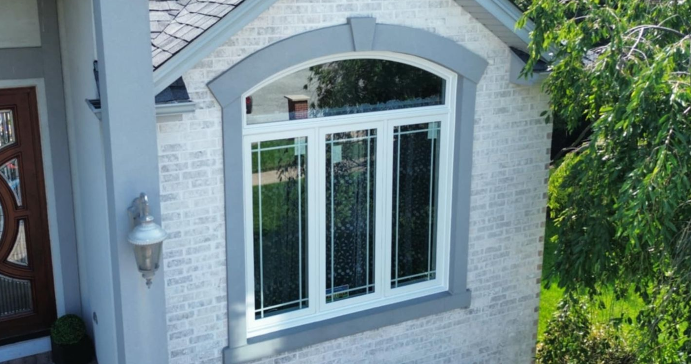 A white brick house with a large arched window. The window has white frames with three vertical panes and a gray trim.