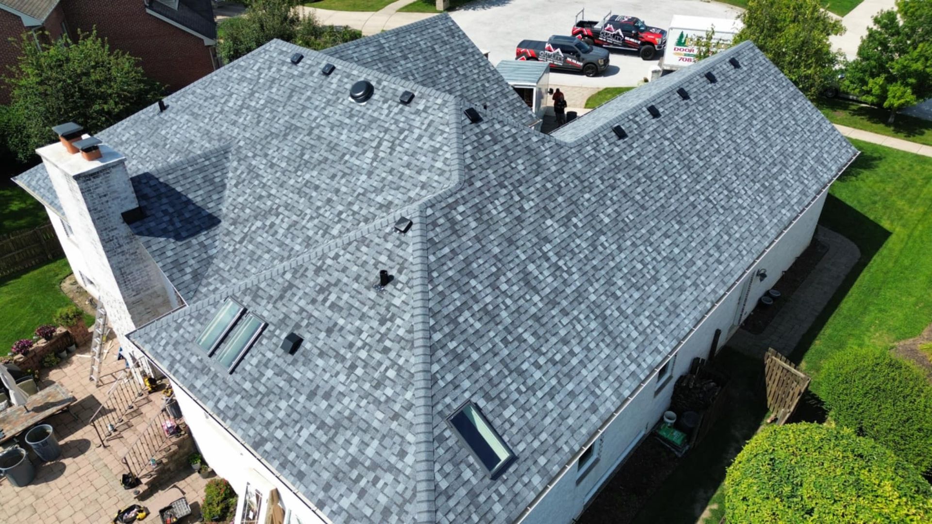 Aerial view of a gray shingle roof on a white house, with green grass surrounding it.