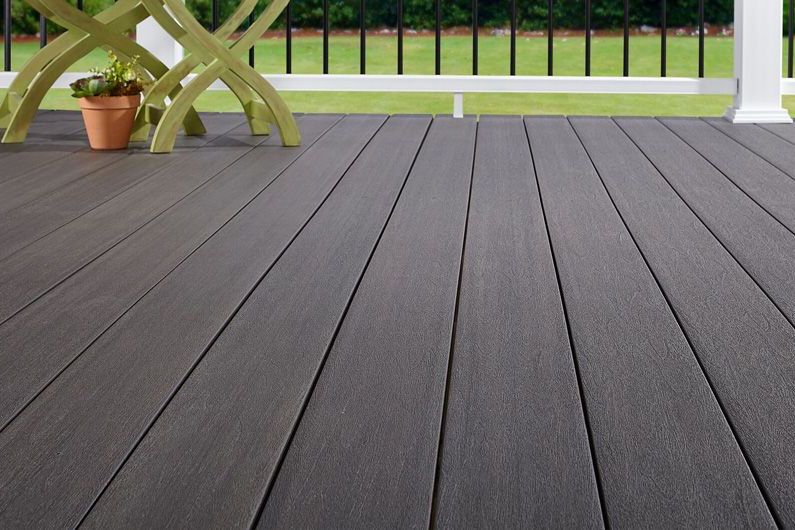 Gray composite deck boards with a green table, flower pot, and black railing.