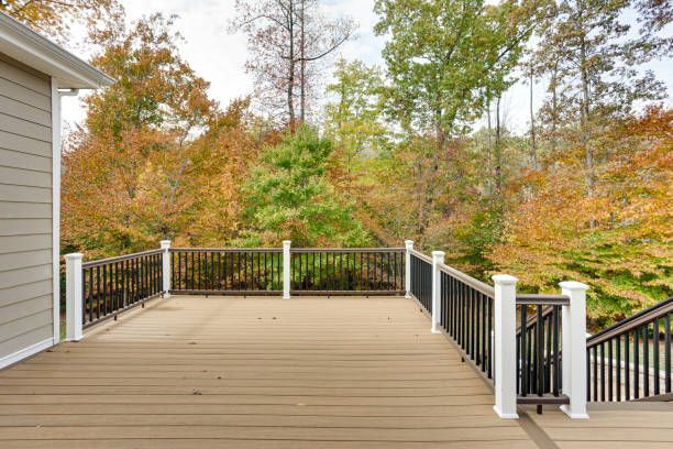 Wooden deck with black railings and white posts, overlooking autumn trees.