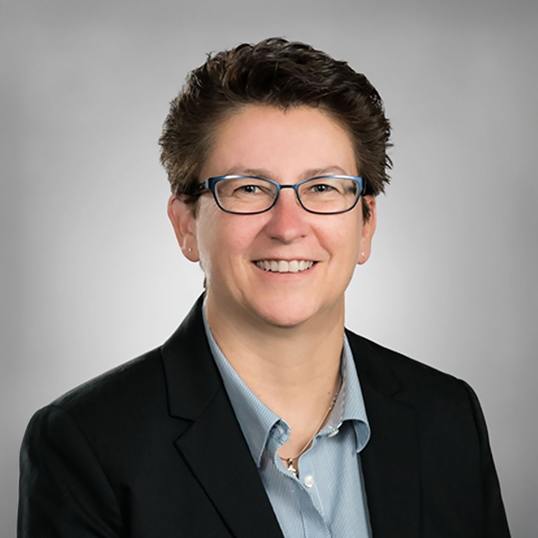 A woman wearing glasses and a black jacket is smiling for the camera.