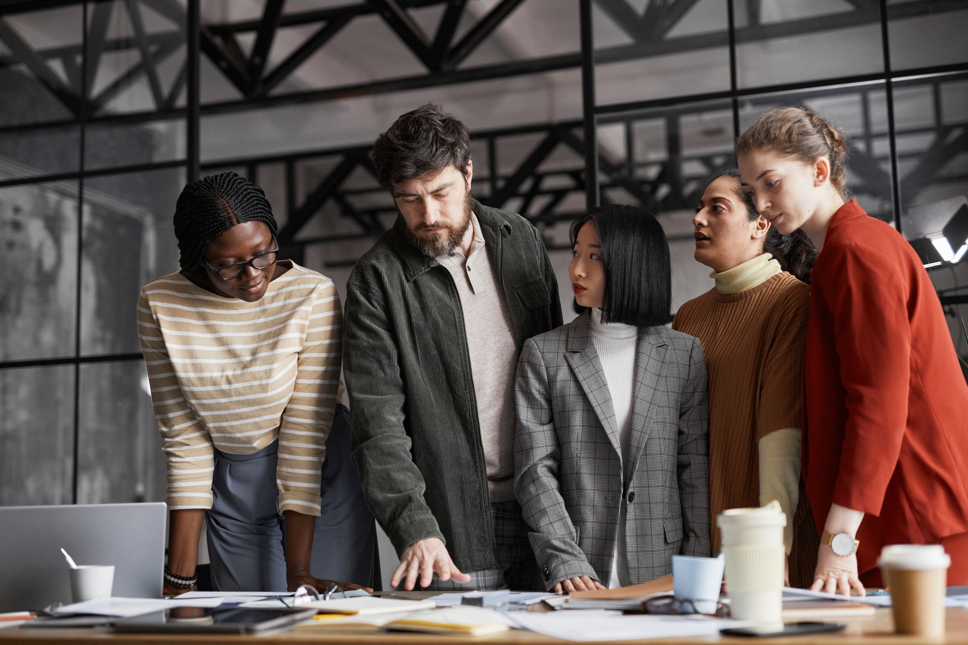 A group of people are standing around a table looking at a laptop.