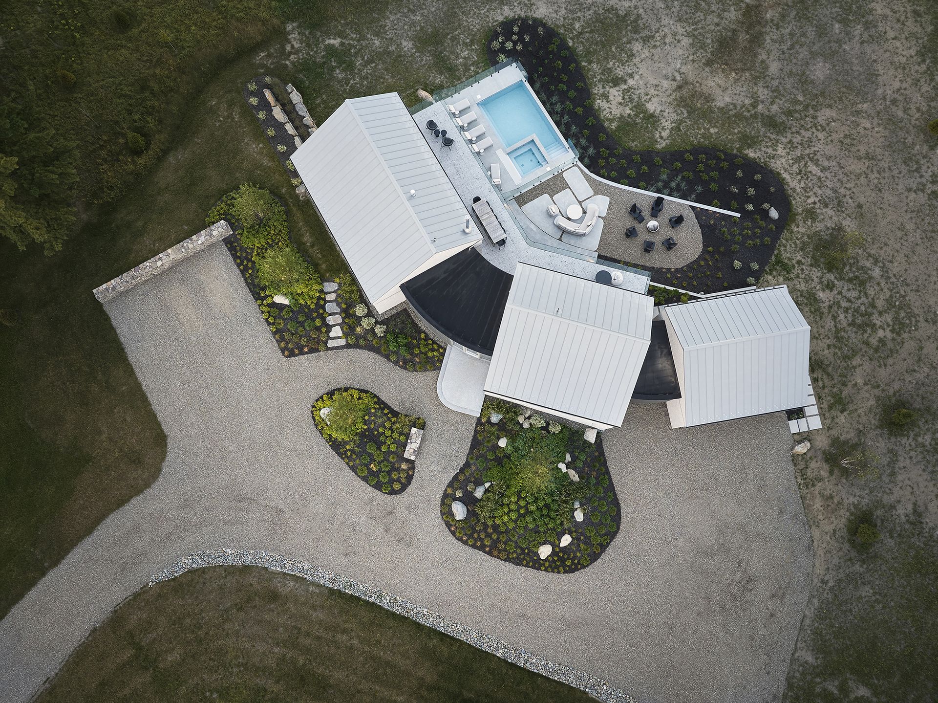 Vue a&eacute;rienne d'une maison blanche moderne avec piscine, all&eacute;e de gravier et am&eacute;nagement paysager environnant.