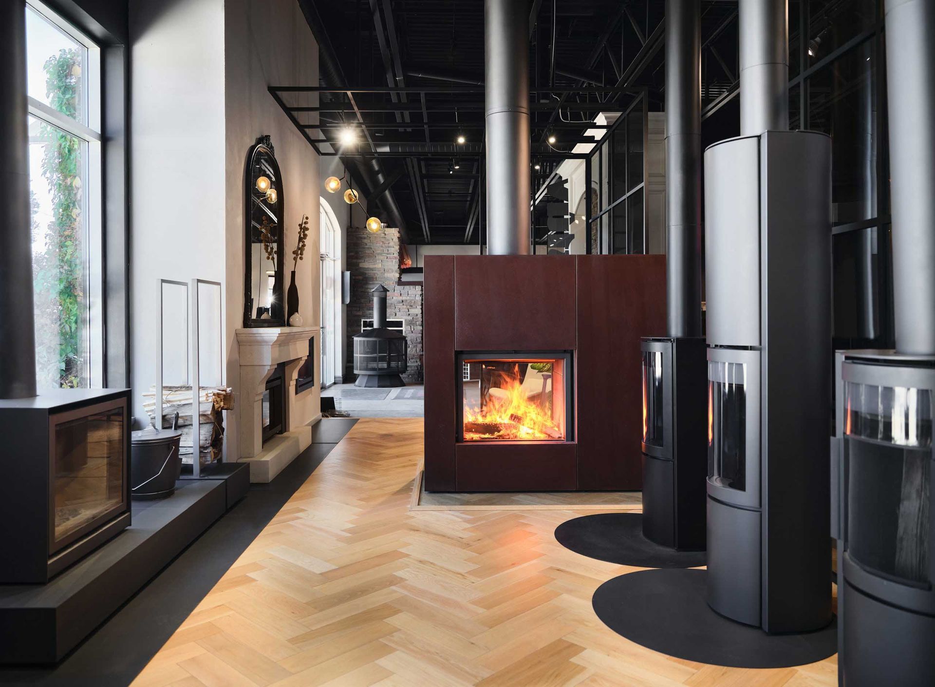 Salle d'exposition de chemin&eacute;es : divers mod&egrave;les de chemin&eacute;es modernes sont expos&eacute;s, certains avec des flammes, sur un sol en bois.