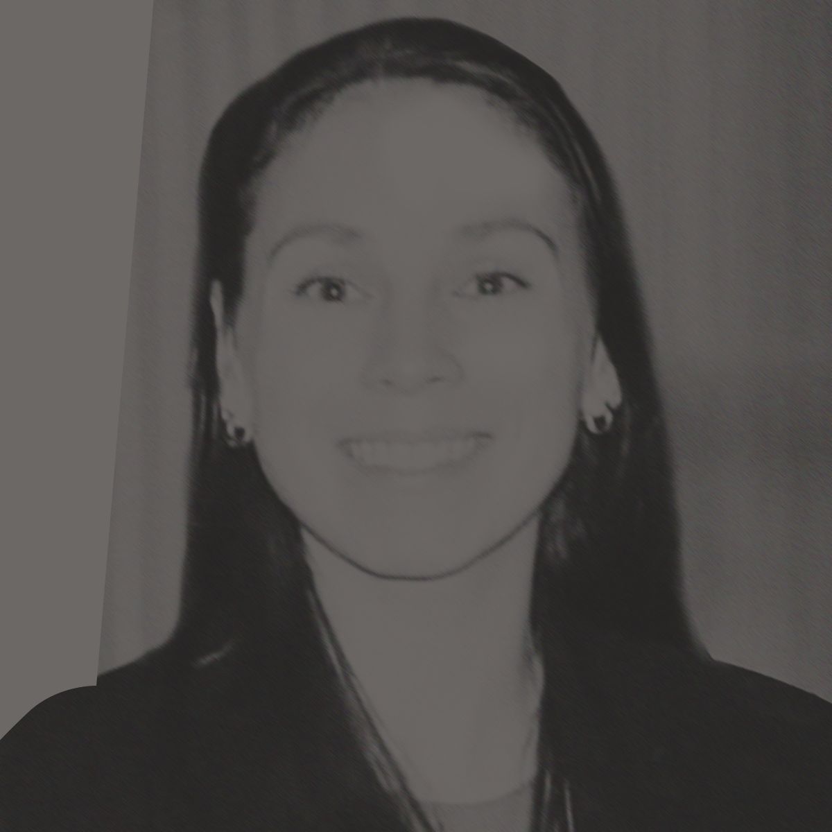 Woman with brown hair smiles, wearing a black blazer and hoop earrings, indoors.