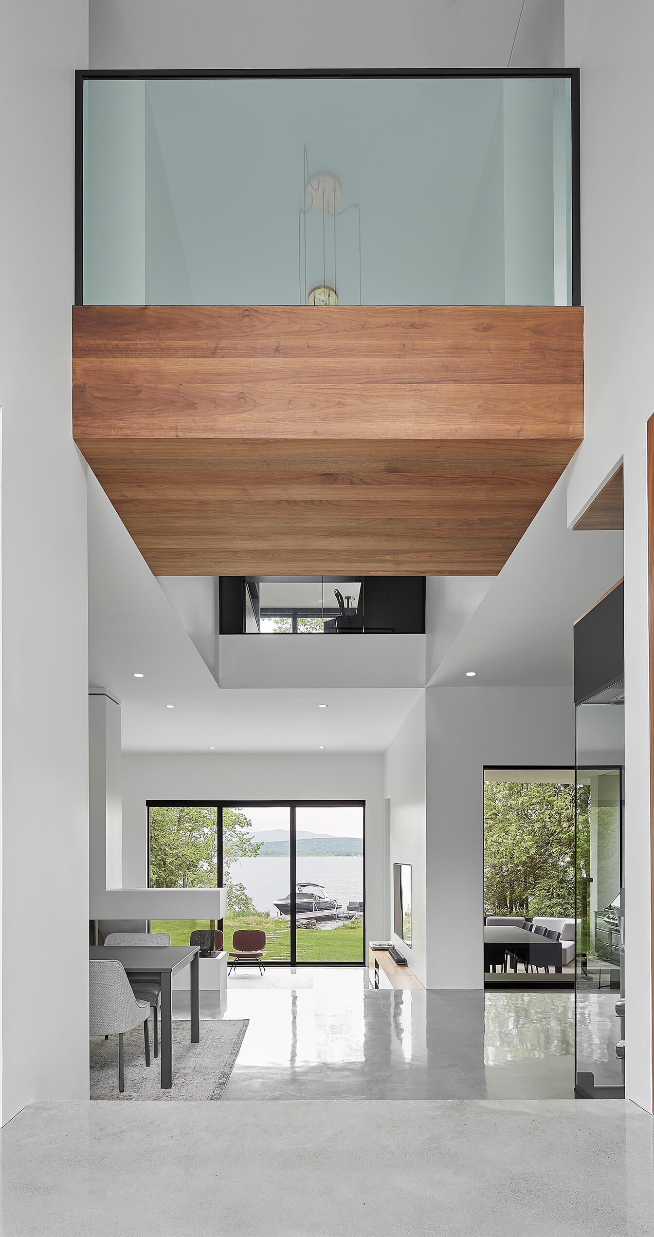 Int&eacute;rieur d'une maison moderne avec balcon en bois et en verre offrant une vue sur l'eau.