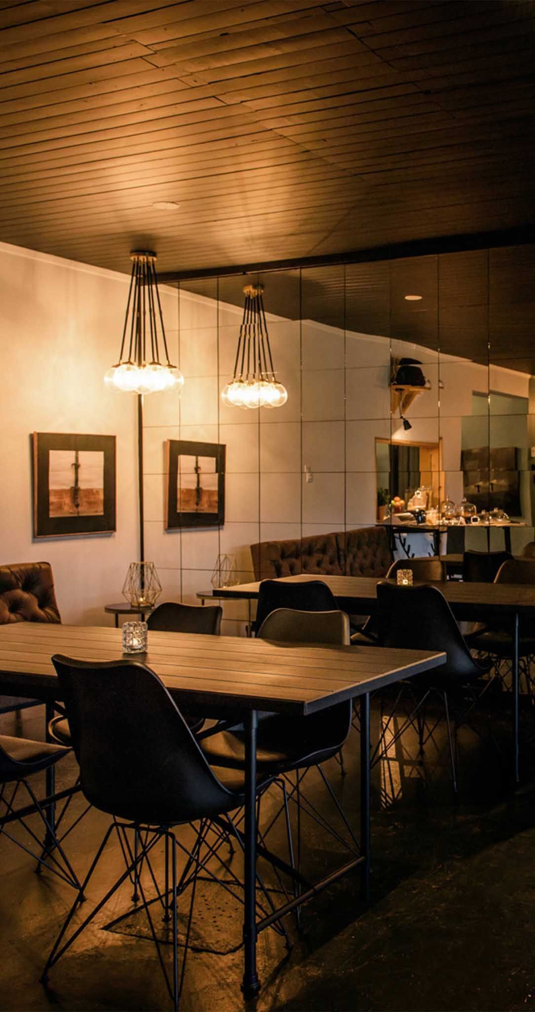 Int&eacute;rieur du restaurant: tables avec chaises, deux tableaux, luminaires et un miroir refl&eacute;tant l&rsquo;espace.