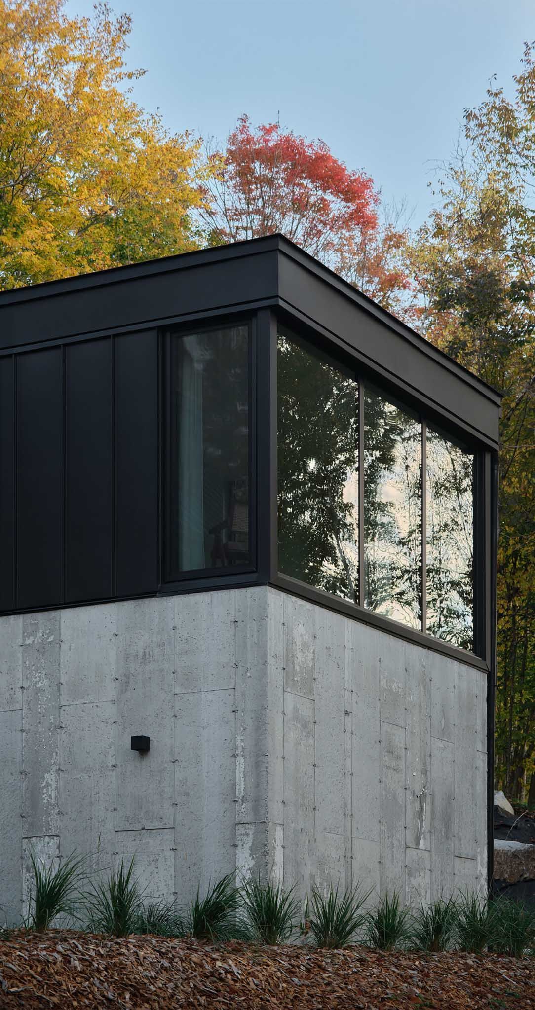 B&acirc;timent moderne avec base en b&eacute;ton et &eacute;tage sup&eacute;rieur noir, de grandes fen&ecirc;tres refl&egrave;tent le feuillage d'automne.