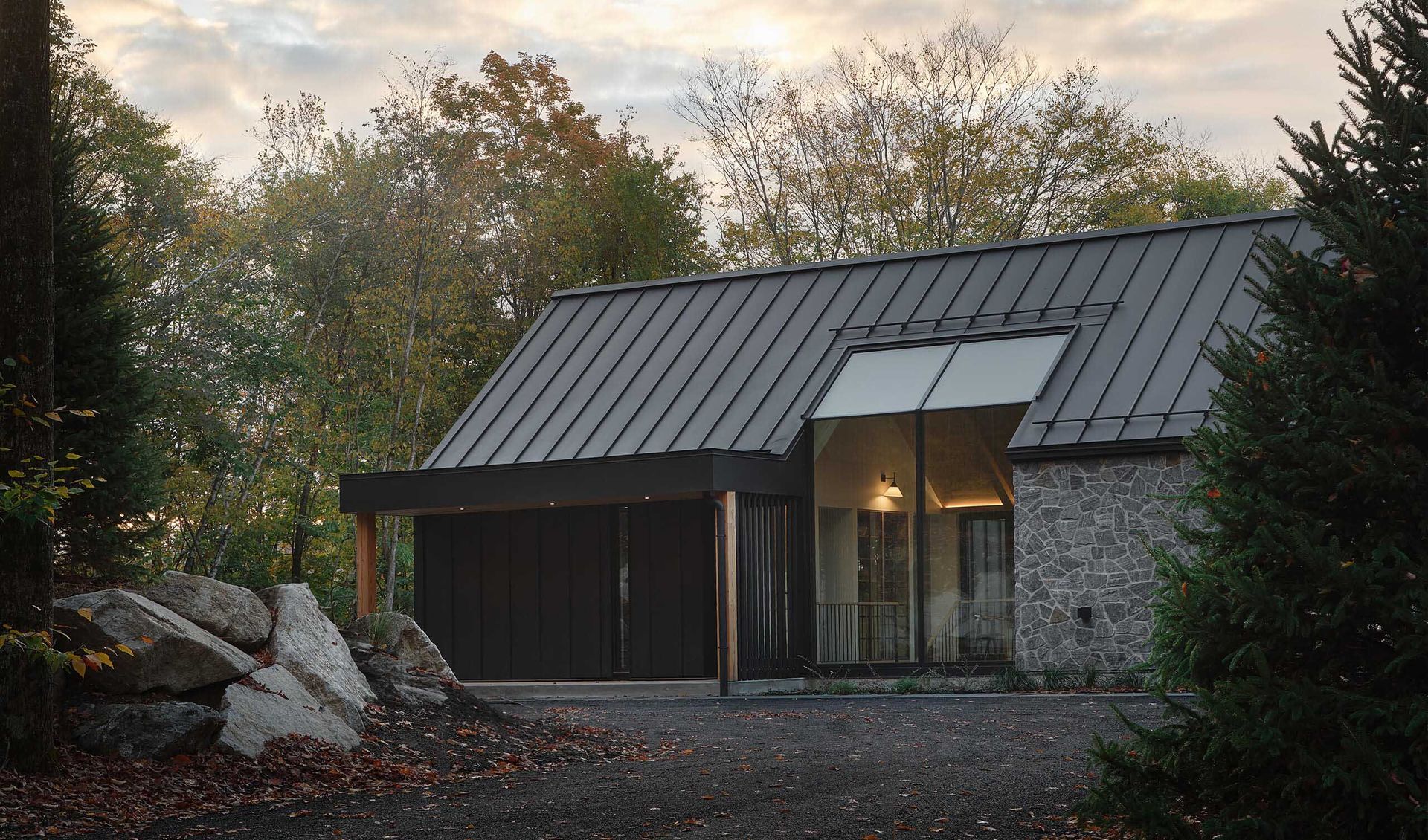 Maison moderne avec un toit en métal sombre et des murs en pierre, entourée d'arbres.