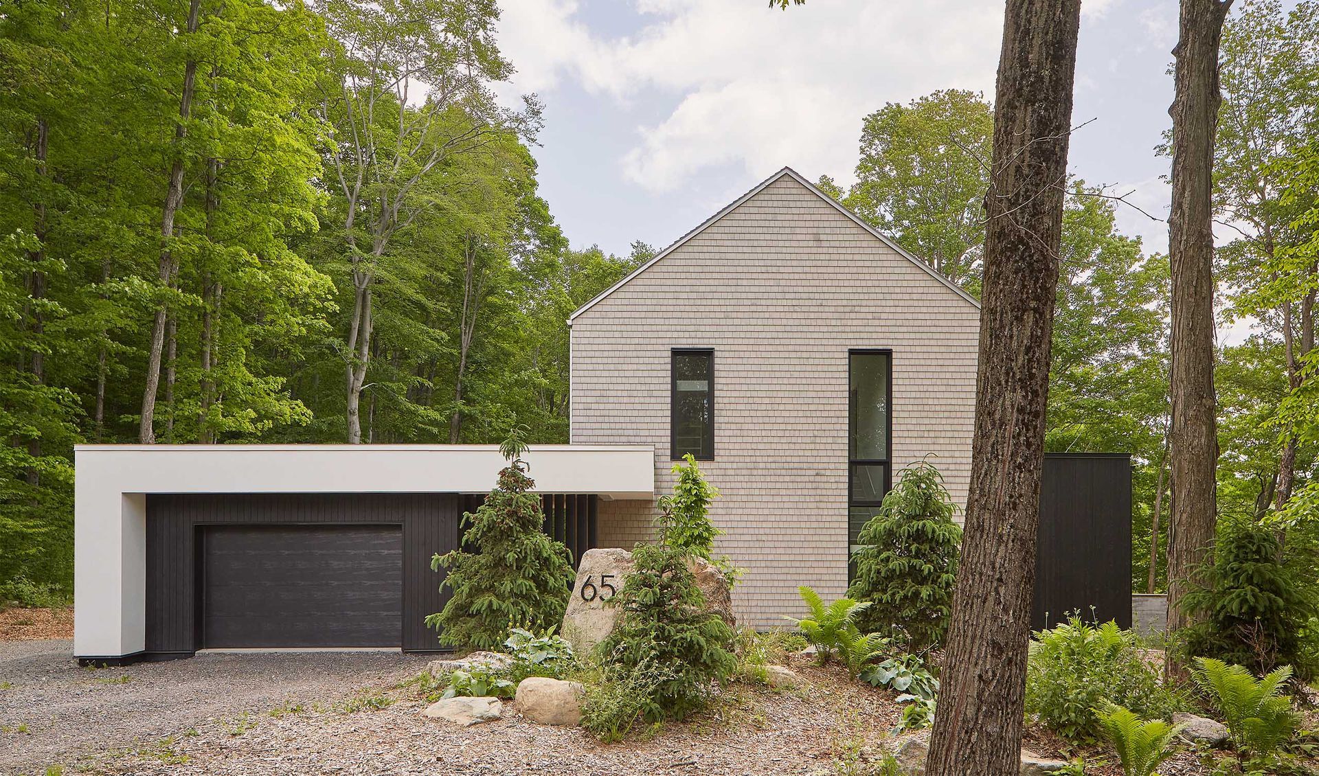 Maison moderne avec façade grise texturée, garage attenant, entourée d'arbres.