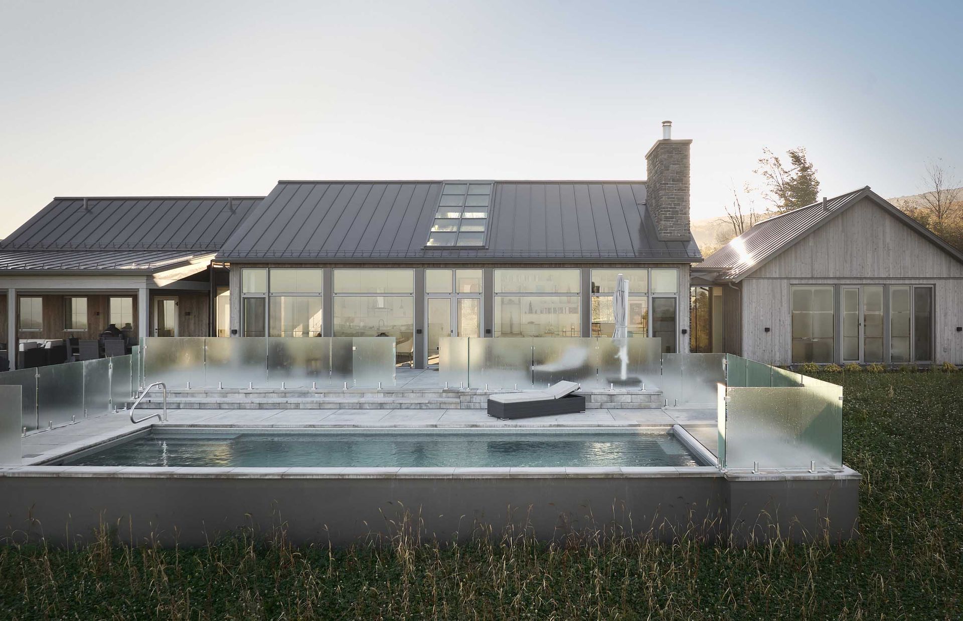 Maison moderne avec piscine, balustrades en verre et chemin&eacute;e ; vue ext&eacute;rieure.
