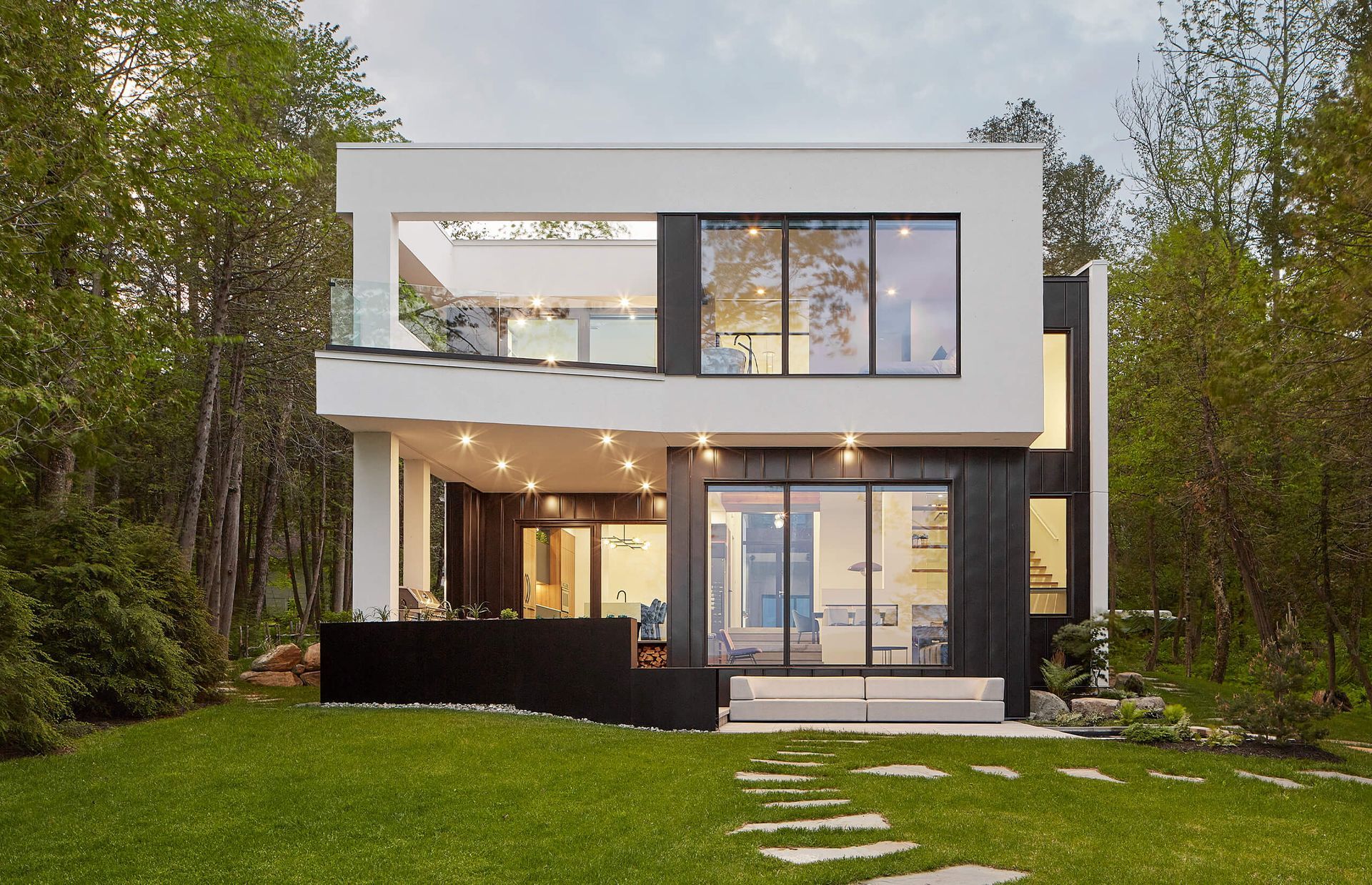 Maison moderne de deux &eacute;tages avec fa&ccedil;ade noire et blanche, grandes fen&ecirc;tres et patio, situ&eacute;e dans un quartier bois&eacute; et verdoyant.