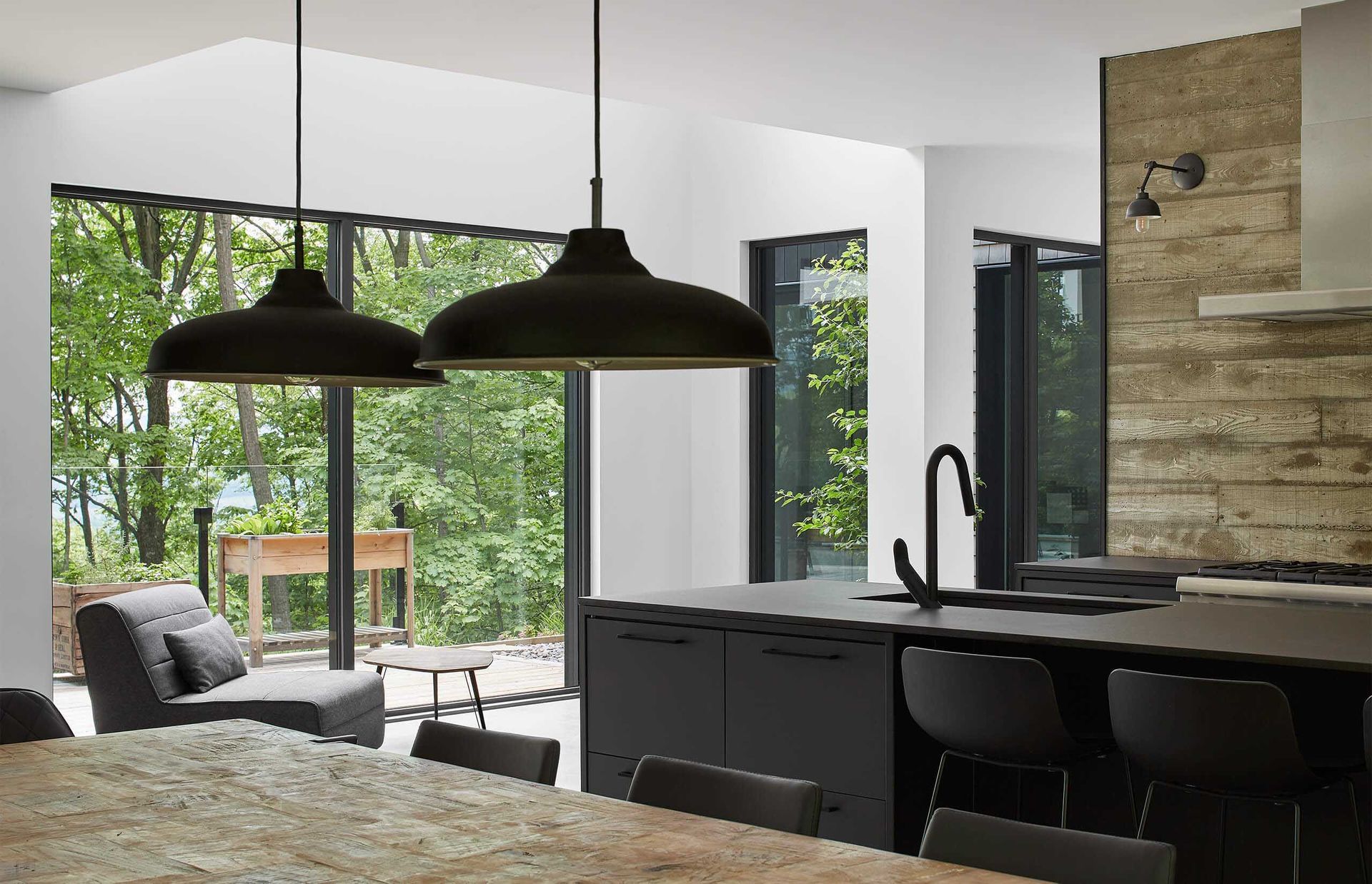 Cuisine moderne avec &icirc;lot central noir, suspensions lumineuses et grandes fen&ecirc;tres donnant sur un paysage verdoyant.