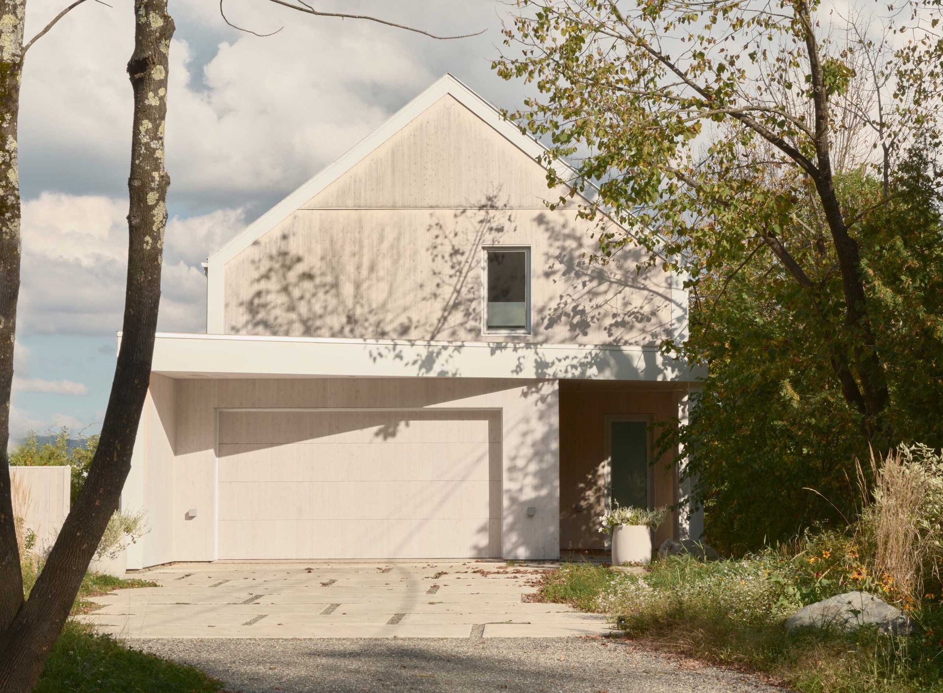 Maison moderne à deux étages avec une façade blanche, un toit à pignon, une porte de garage et une allée en béton.
