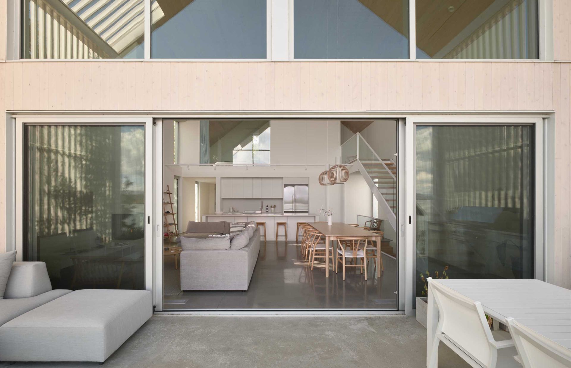 Vue ext&eacute;rieure d'une maison blanche moderne avec de grandes portes coulissantes en verre s'ouvrant sur un espace de vie.