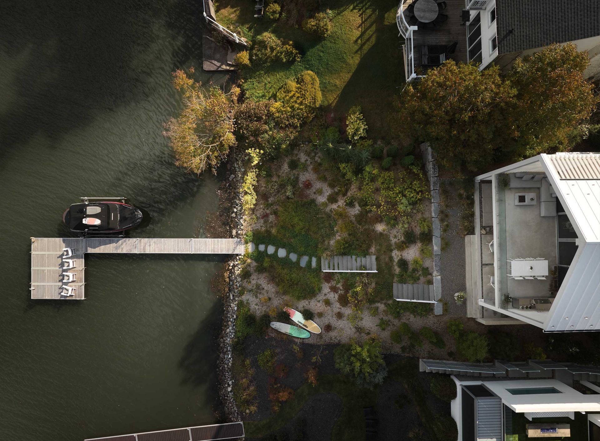 Vue a&eacute;rienne d'un quai avec un bateau, des kayaks et une maison moderne au bord d'un lac.