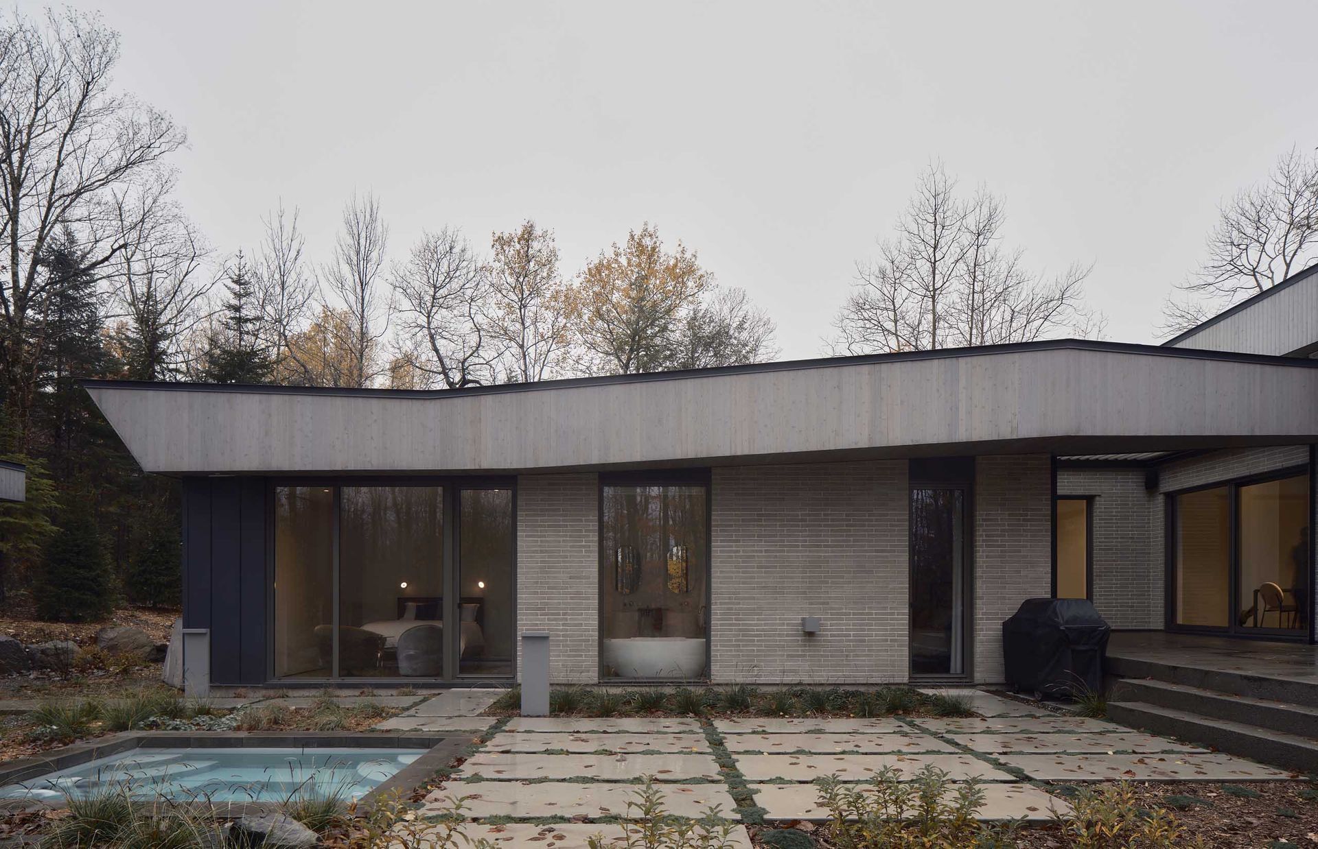 Ext&eacute;rieur de maison moderne avec piscine, murs de verre et toit incurv&eacute;.