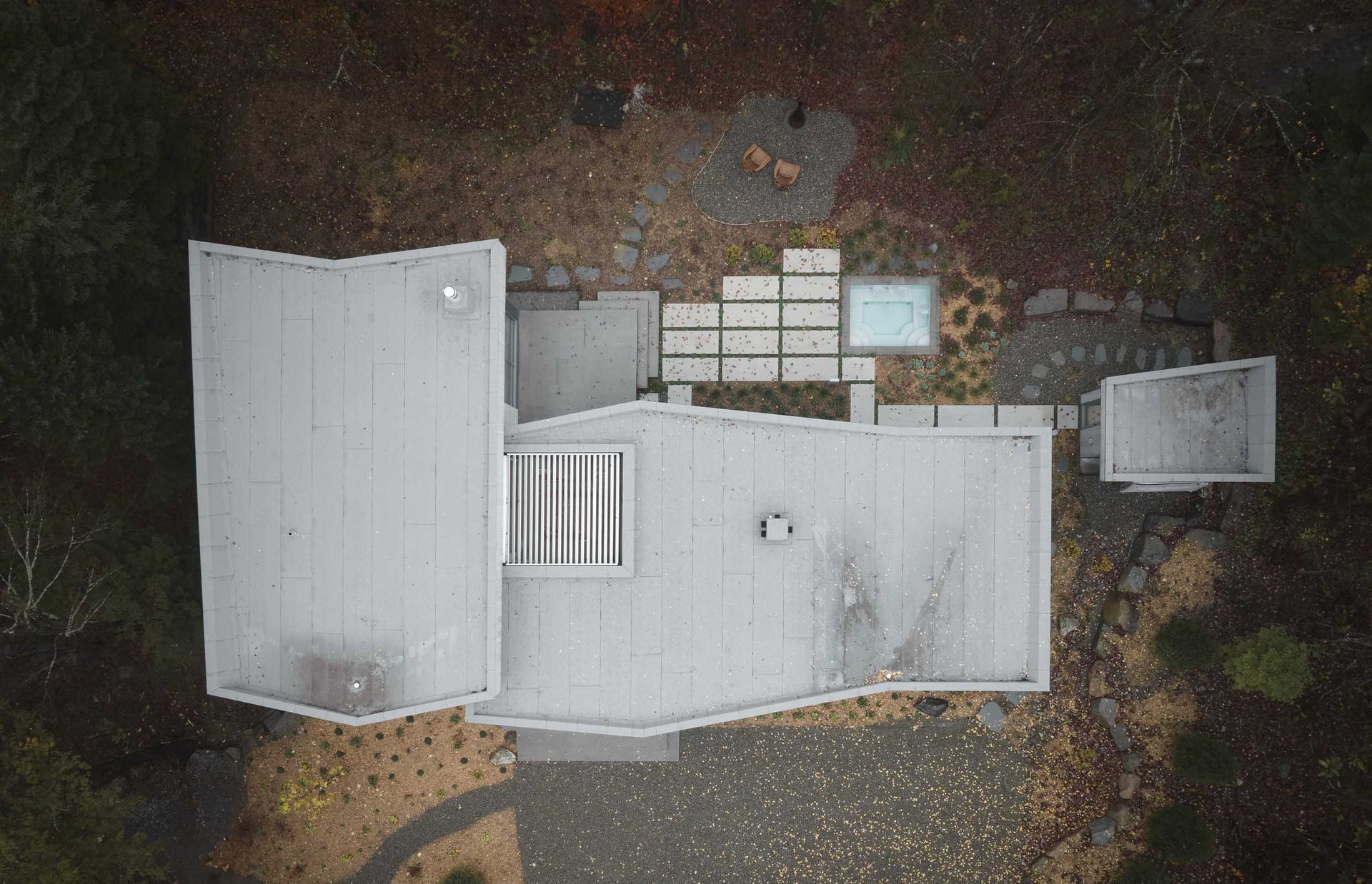 Vue a&eacute;rienne d'une maison moderne au toit gris, avec terrasse et jacuzzi, le tout entour&eacute; d'un cadre naturel.