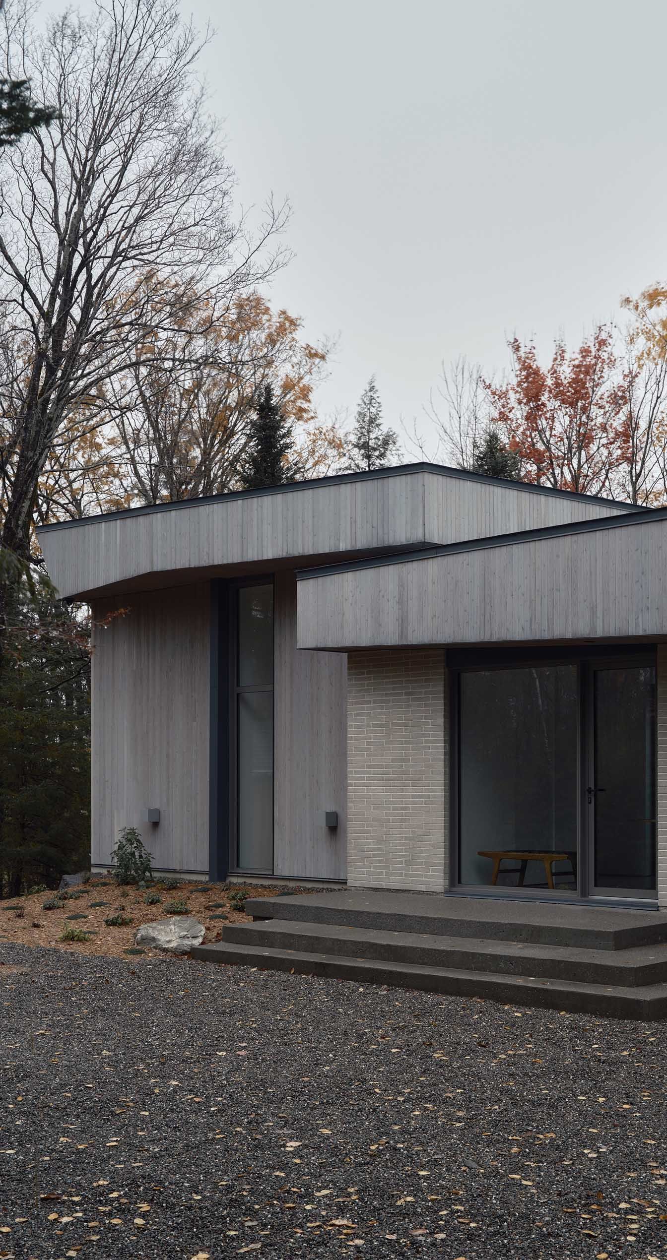 B&acirc;timent moderne aux tons clairs, avec des murs incurv&eacute;s et des fen&ecirc;tres en verre, entour&eacute; d'arbres et de gravier.