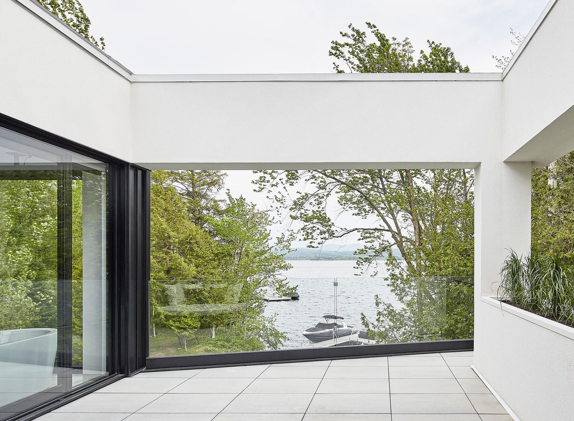Balcon donnant sur un lac, des arbres et des bateaux ; murs blancs, carrelage gris.