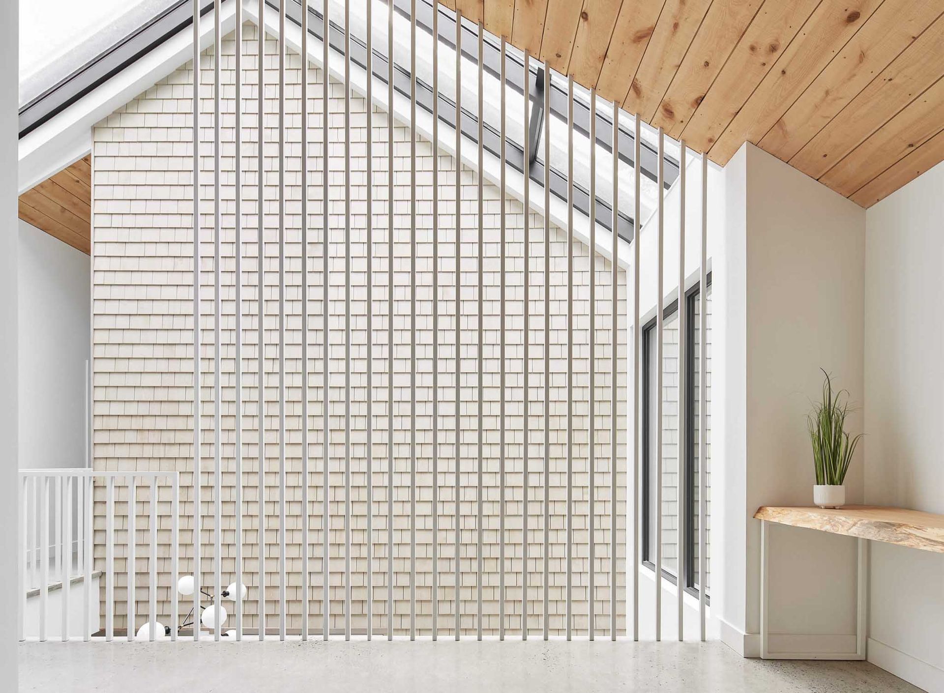 Vue intérieure d'une maison moderne avec des lattes blanches verticales, un plafond en bois et un petit bureau avec une plante.