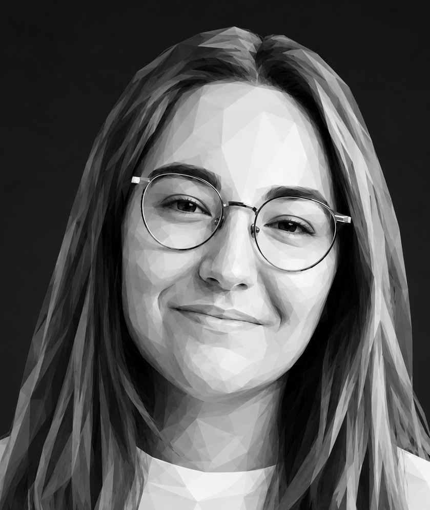 Femme souriante portant des lunettes et un t-shirt blanc. Longs cheveux bruns, à l'intérieur, poutres apparentes.