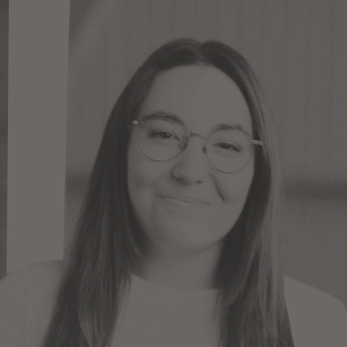 Woman with long brown hair, round glasses, and a slight smile, wearing a white shirt; indoors.
