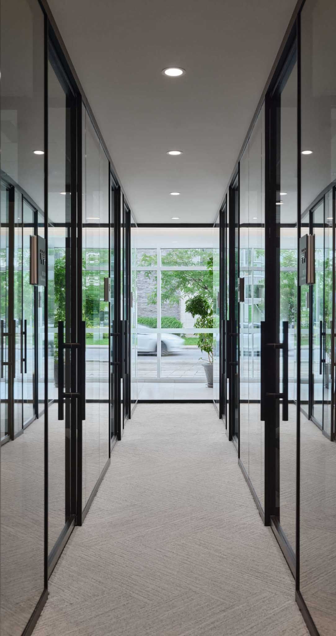 Couloir de bureaux &eacute;troit bord&eacute; de pi&egrave;ces aux parois vitr&eacute;es donnant sur l'ext&eacute;rieur.
