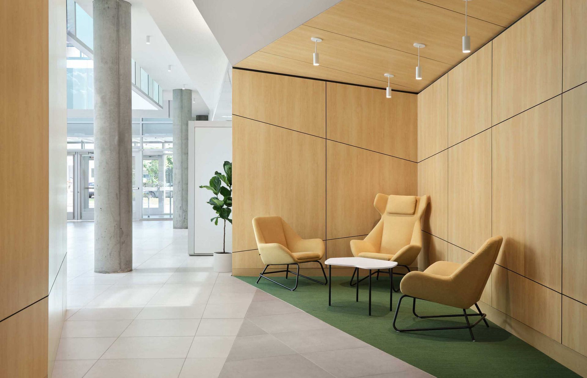 Hall d'entr&eacute;e moderne avec boiseries claires, chaises jaunes et petite table ronde. Moquette verte.