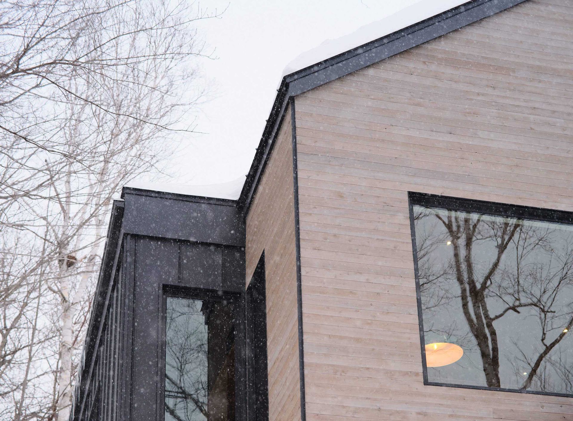 Fa&ccedil;ade d'un b&acirc;timent moderne avec bardage en bois, finitions noires et grandes fen&ecirc;tres. Sc&egrave;ne d'hiver enneig&eacute;e.