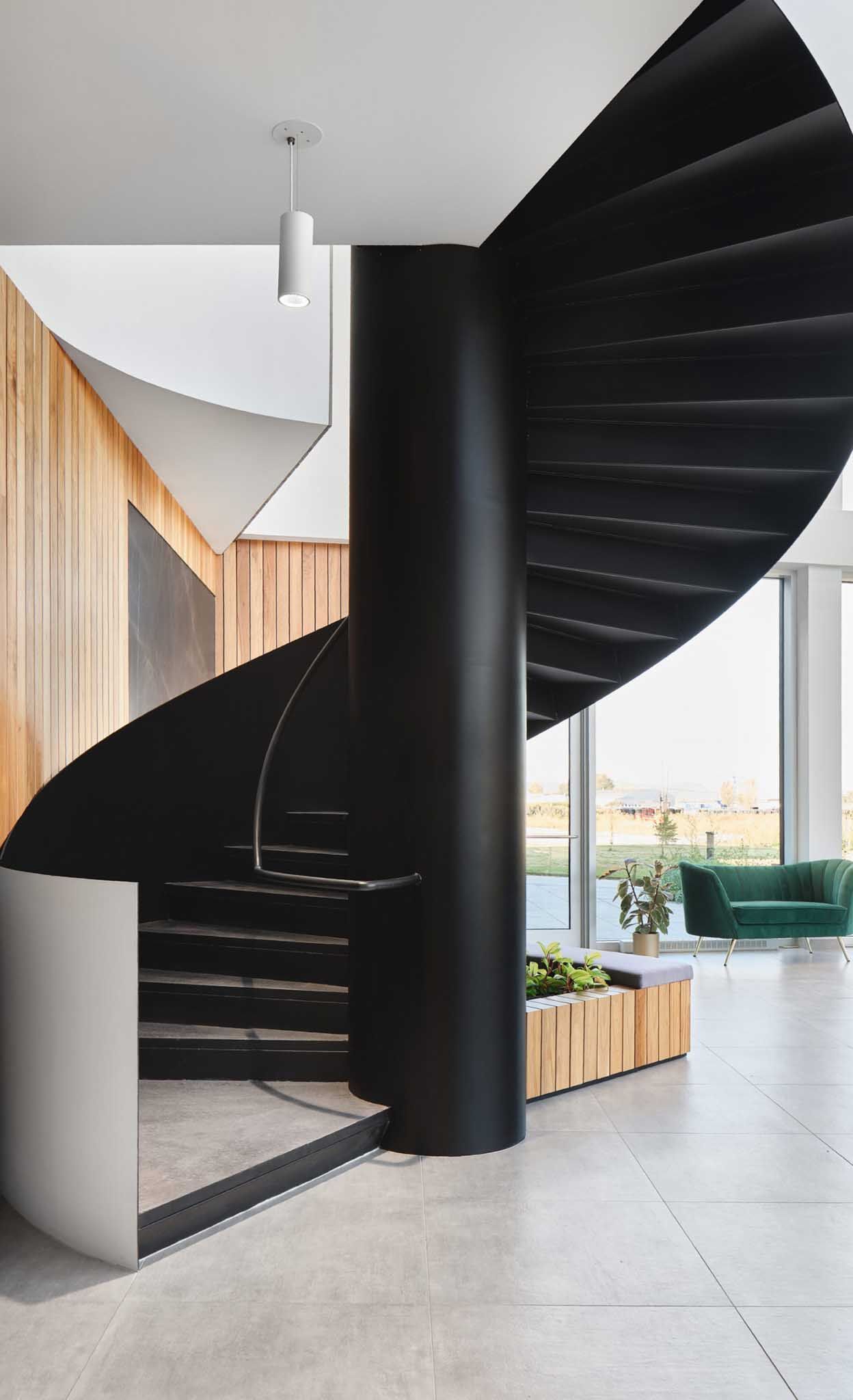 Black spiral staircase with central column, wood paneling, and a green sofa.
