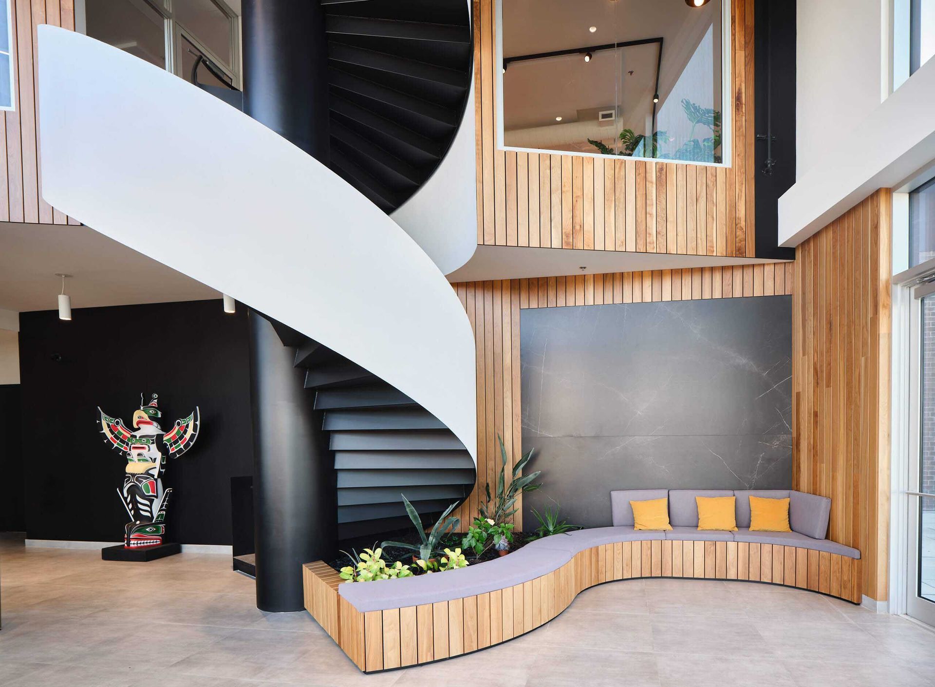 Int&eacute;rieur moderne avec escalier en colima&ccedil;on, boiseries, coin salon avec coussins jaunes et totem am&eacute;rindien.