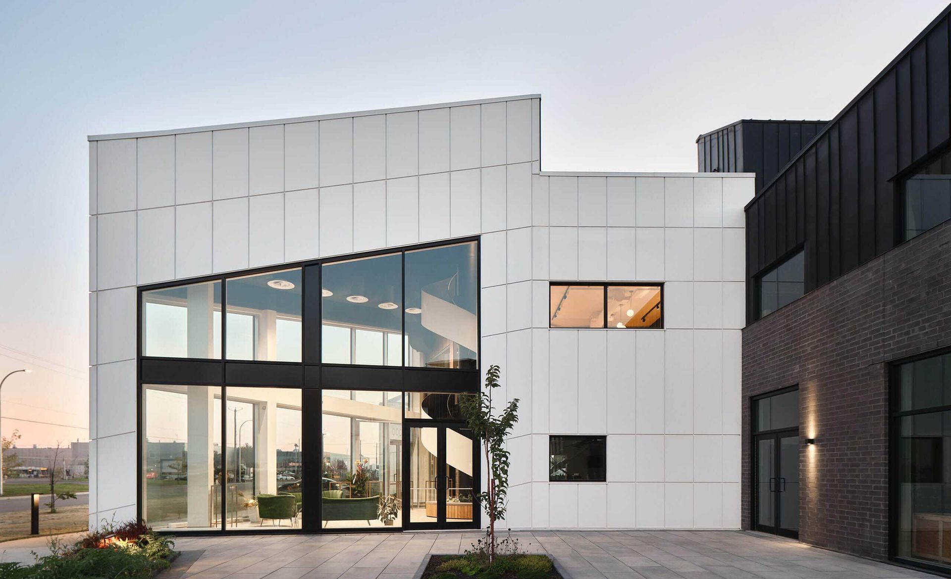 B&acirc;timent moderne avec fa&ccedil;ade blanche et noire, grandes baies vitr&eacute;es et entr&eacute;e pav&eacute;e.