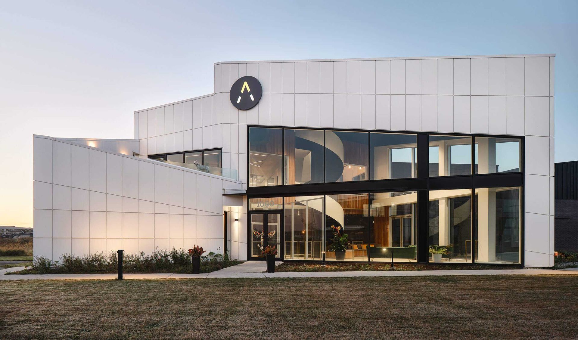 B&acirc;timent moderne blanc avec de grandes baies vitr&eacute;es et un logo en forme de &laquo; A &raquo;.