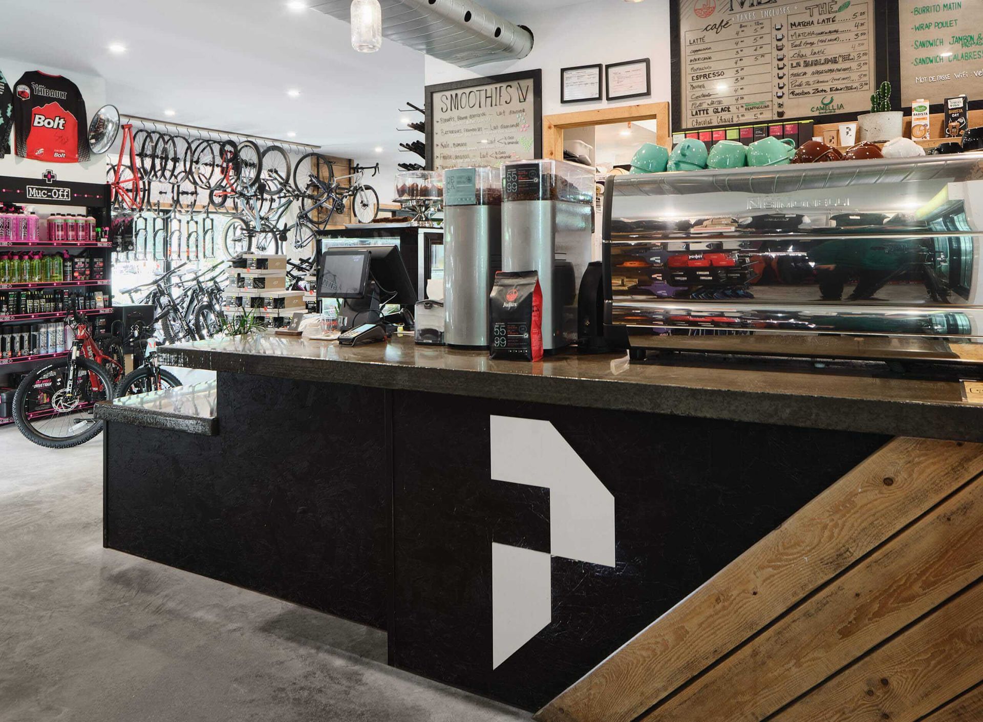Bar &agrave; caf&eacute; &agrave; l'int&eacute;rieur d'un magasin de v&eacute;los. Machine &agrave; expresso en acier inoxydable, menu, v&eacute;los accroch&eacute;s au mur.