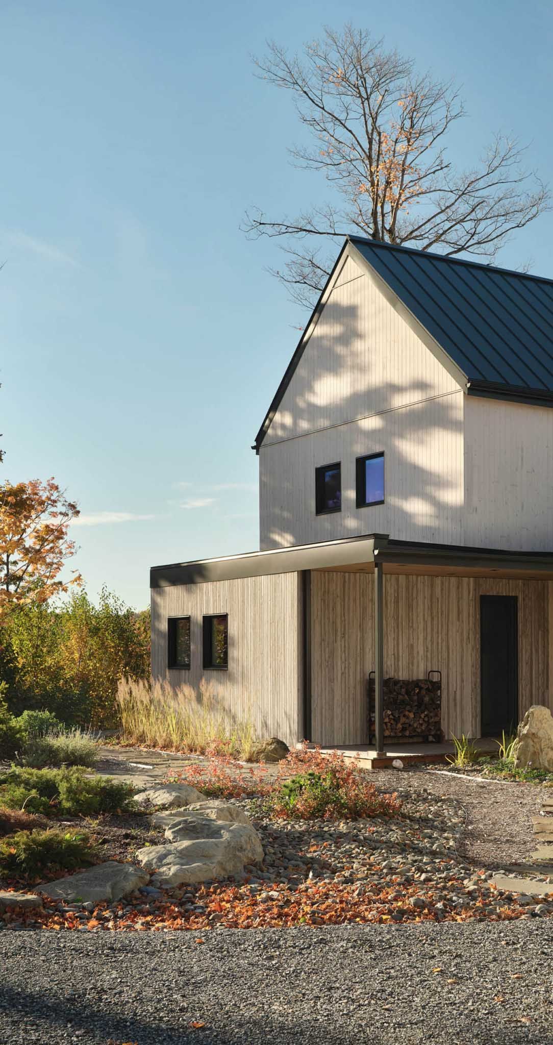 Maison en bois &agrave; deux &eacute;tages, toit sombre et porche, entour&eacute;e de feuillage d'automne, par une journ&eacute;e ensoleill&eacute;e.