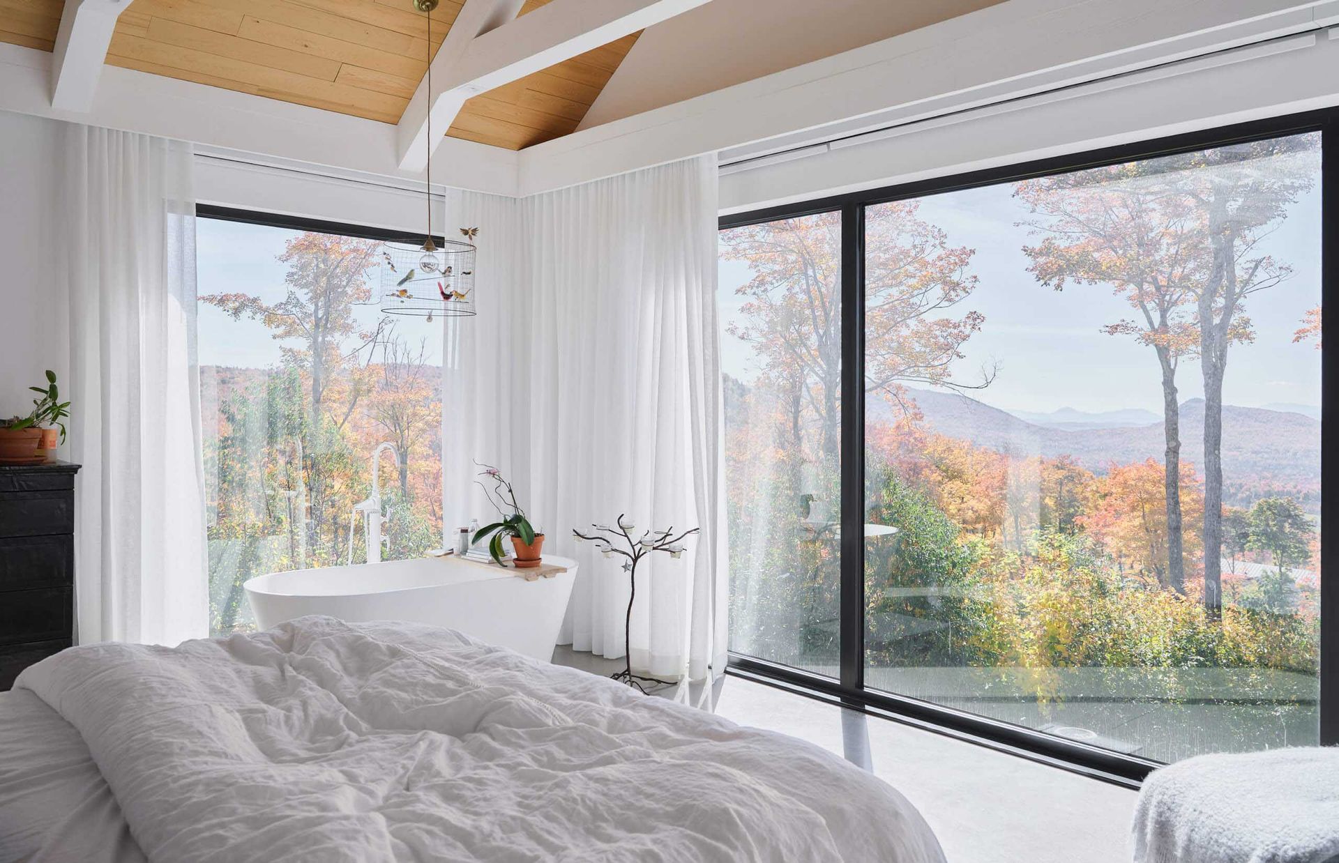 Chambre avec grandes fen&ecirc;tres, vue sur la montagne, lit blanc, baignoire, arbres aux couleurs d'automne.