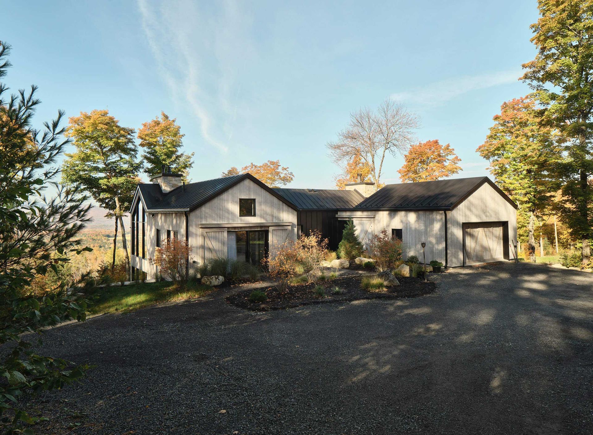 Maison moderne aux tons clairs, avec toit et garage fonc&eacute;s, all&eacute;e de gravier, entour&eacute;e d'arbres aux feuilles d'automne.