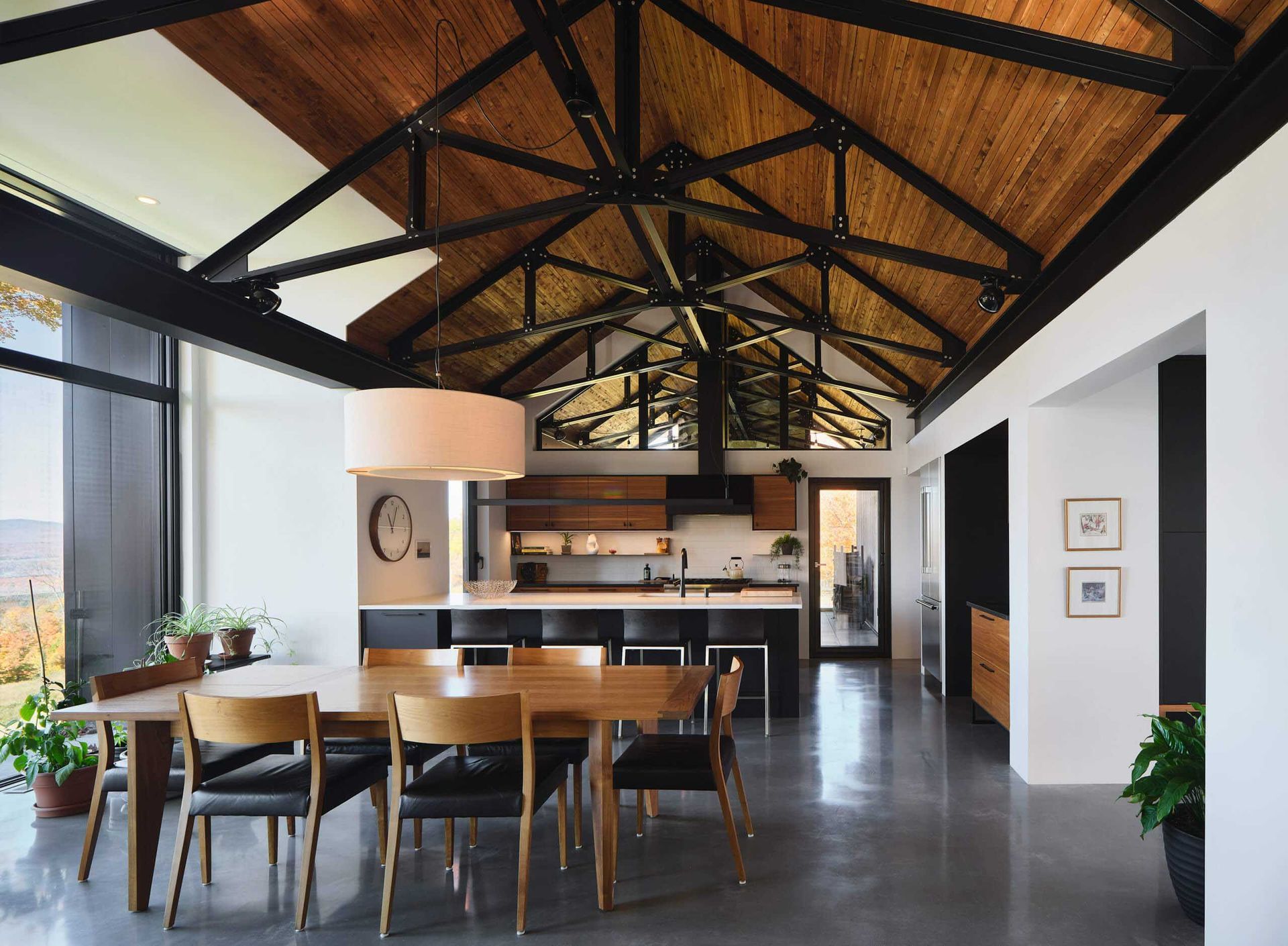 Salle &agrave; manger avec table et chaises en bois, plafond vo&ucirc;t&eacute; avec poutres apparentes et grand luminaire suspendu.