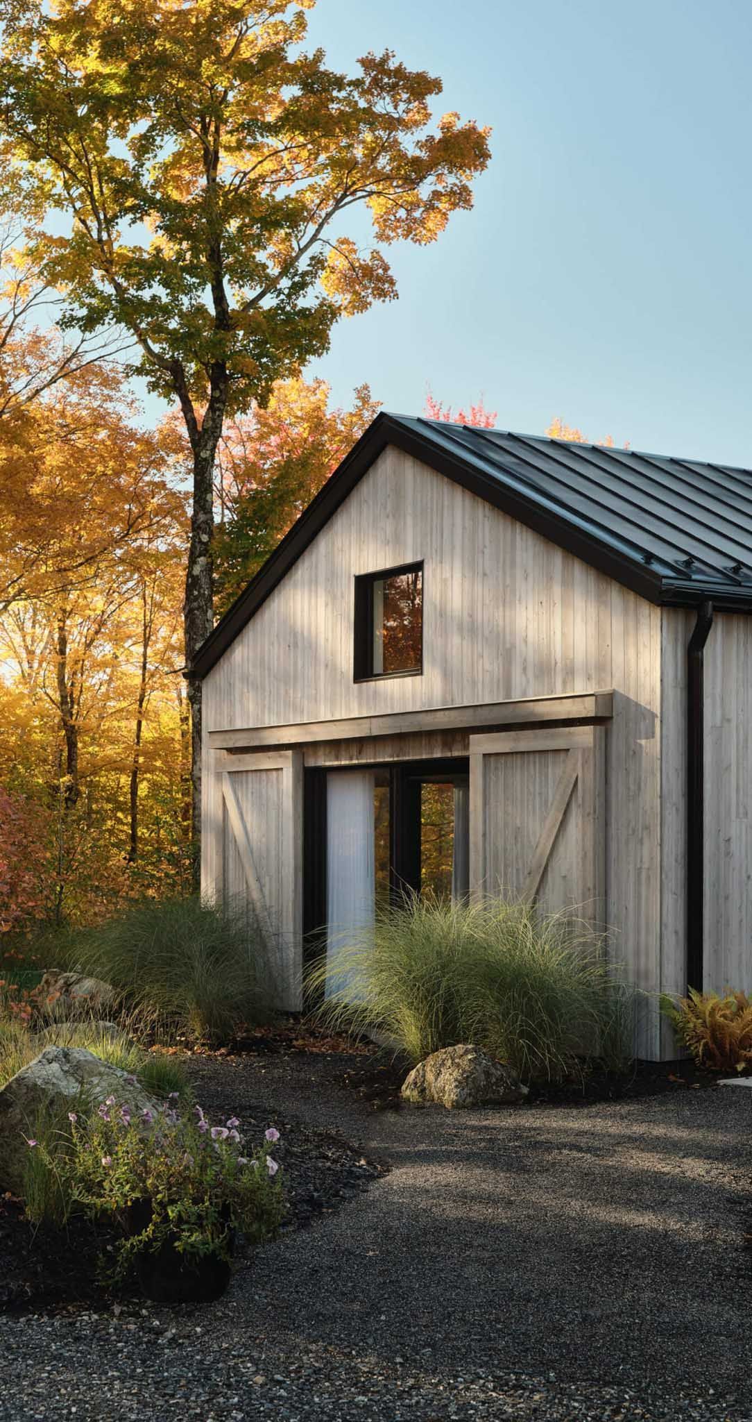 Wooden barn-style building with open sliding doors, surrounded by autumn foliage and gravel pathway.