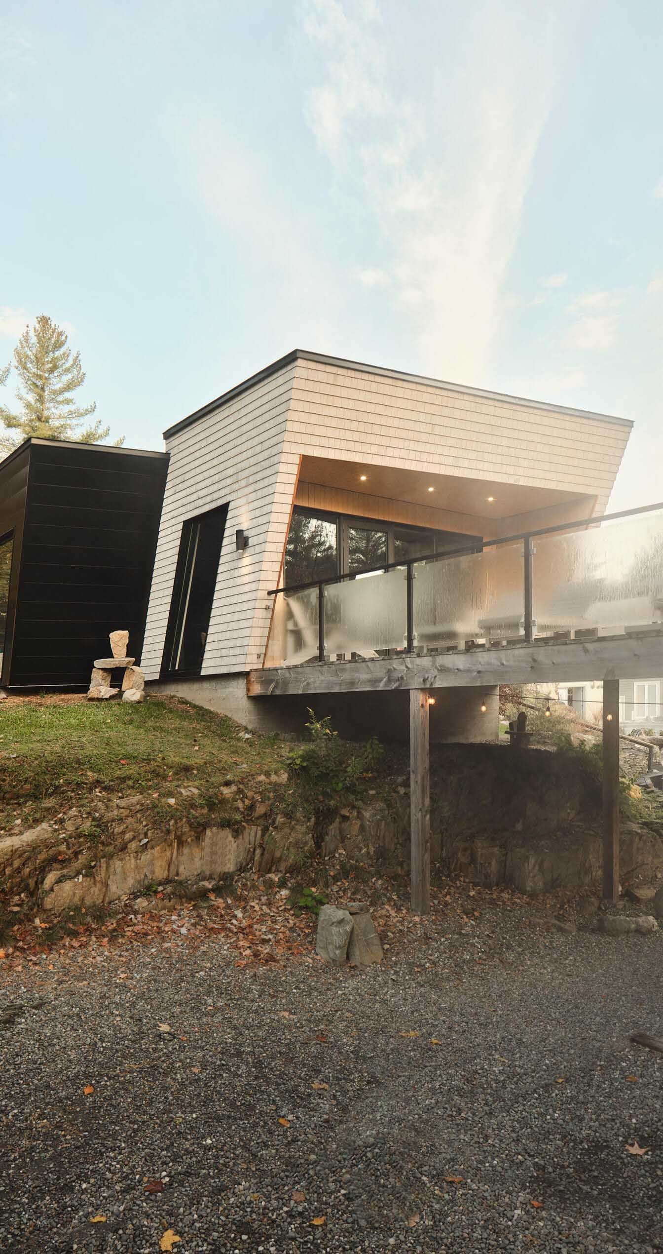 Chalet moderne avec toit en pente, rambarde en verre, terrasse en bois et bardage noir.