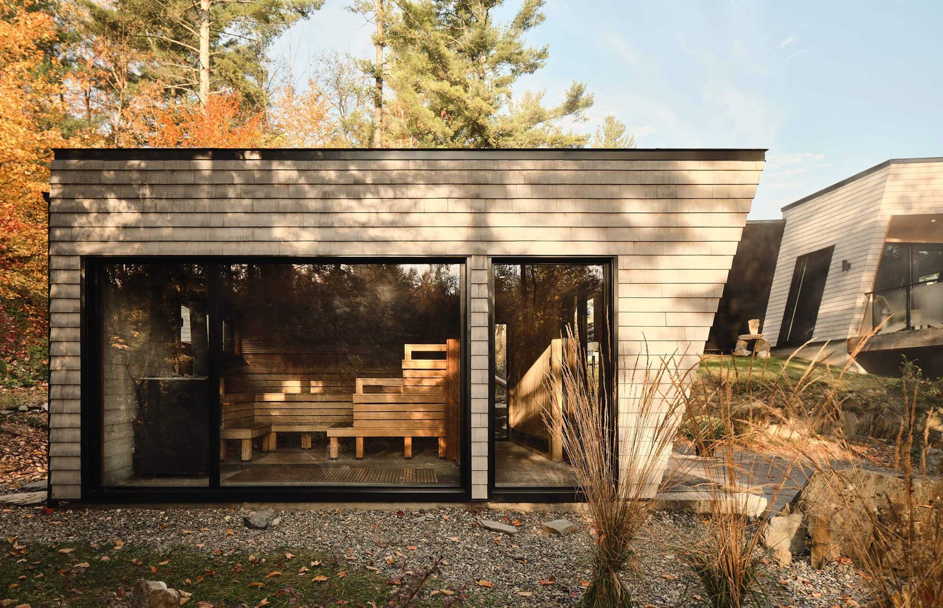 Sauna en bois avec de grandes baies vitrées ; vue extérieure. Paysage automnal avec des arbres.