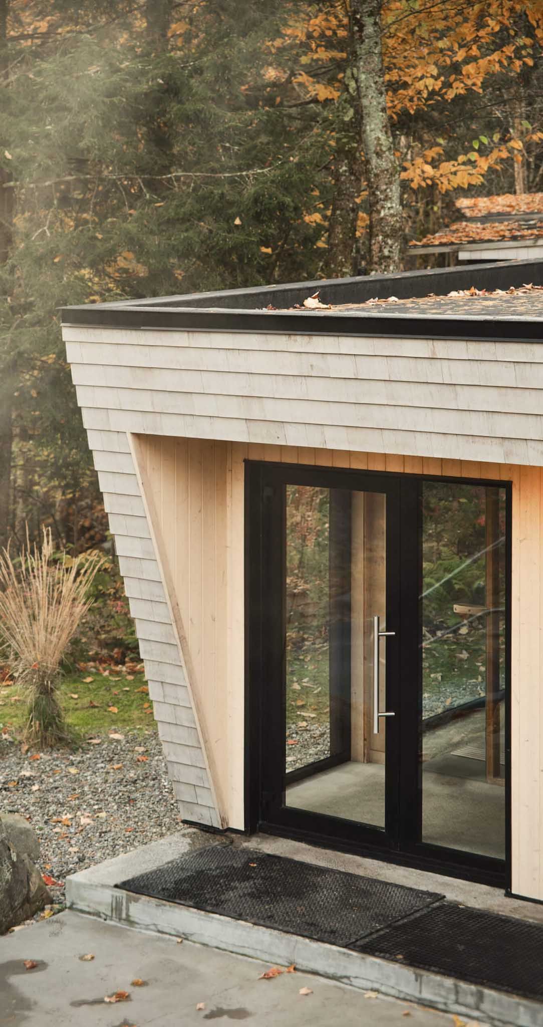 Building with black-framed glass doors and gray roof, surrounded by fall foliage.