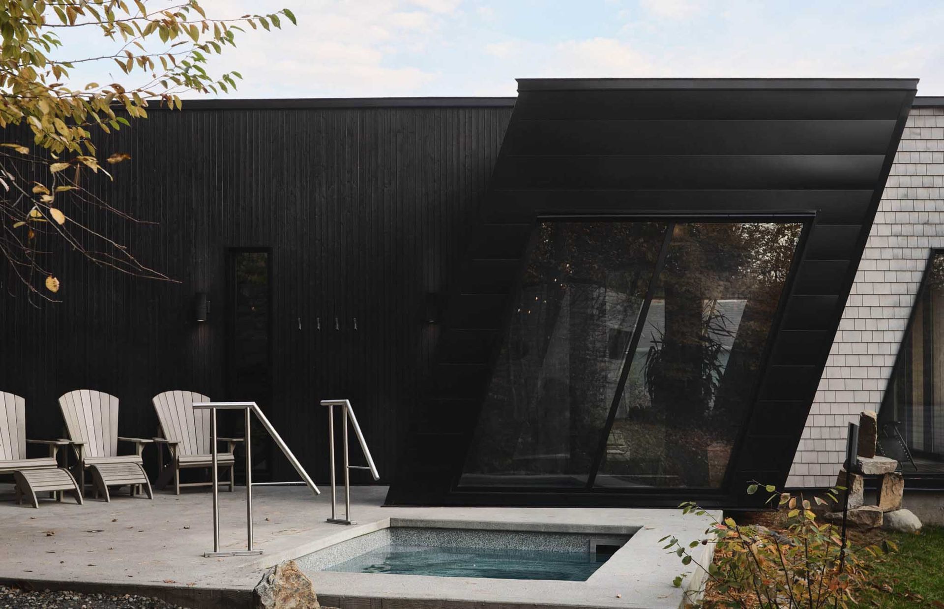 Black building with pool, chairs, and large angled window. Exterior spa scene.
