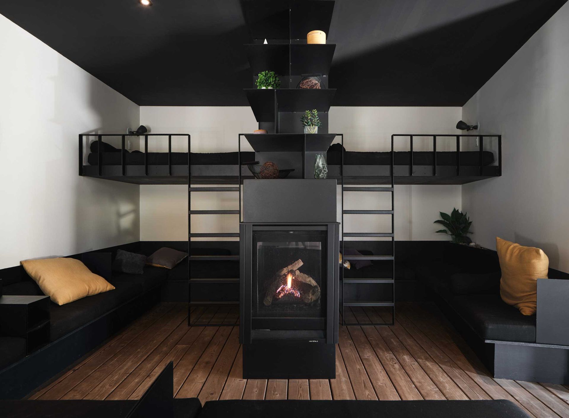 Chambre moderne avec chemin&eacute;e noire, deux lits sur&eacute;lev&eacute;s et canap&eacute;s noirs.