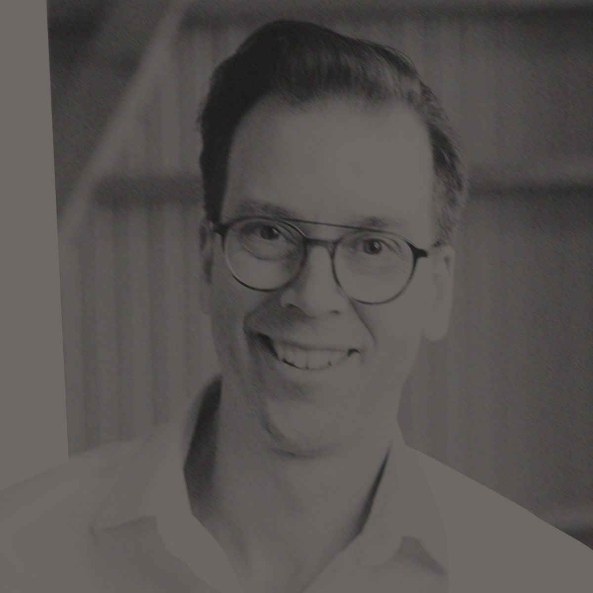 Man with glasses smiles, wearing white shirt, indoors, background of wood and metal.