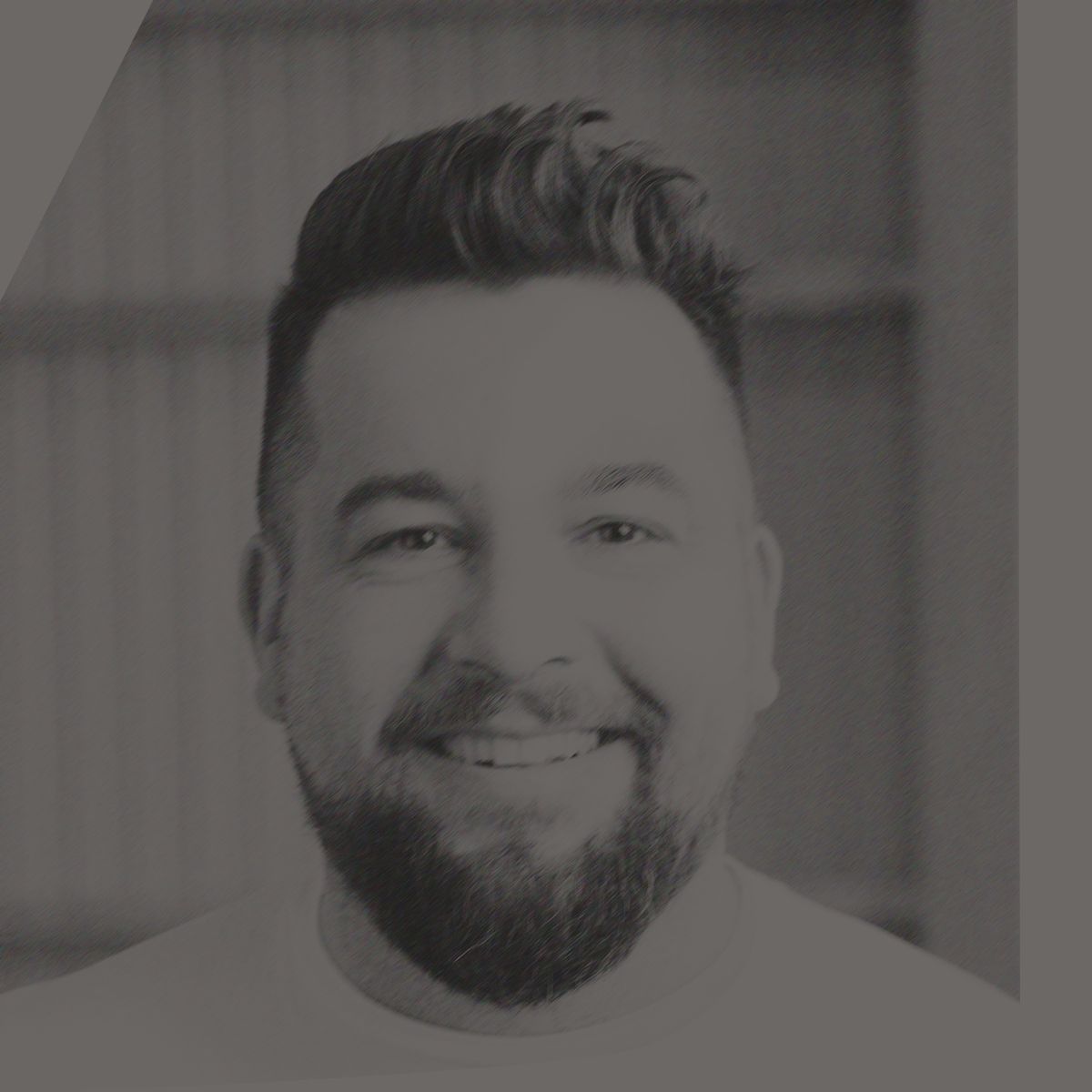 Man with a beard smiling, wearing a white shirt, in a wood-paneled building.