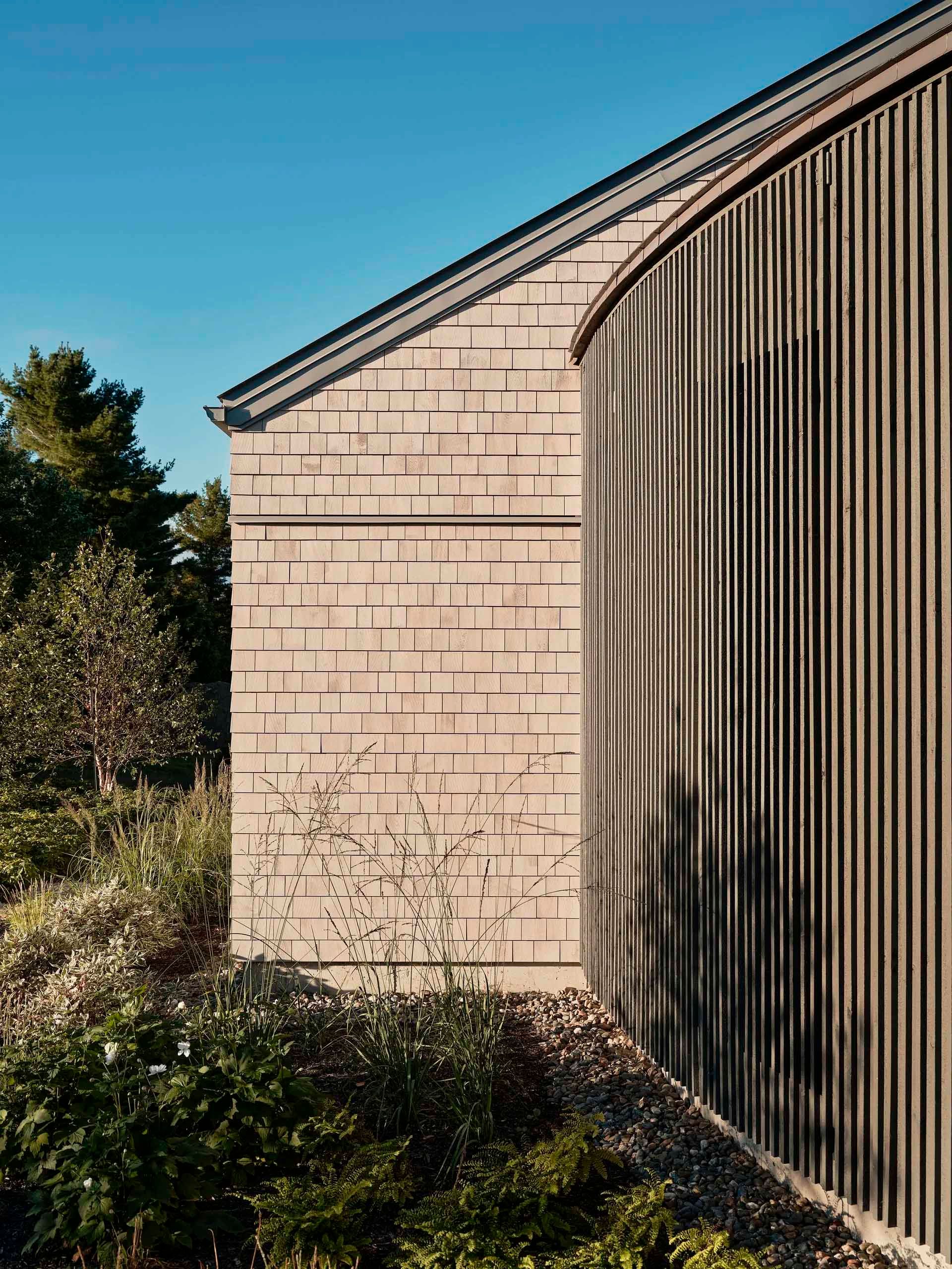 Exterior of building with shingle siding and curved, vertical wood panels.